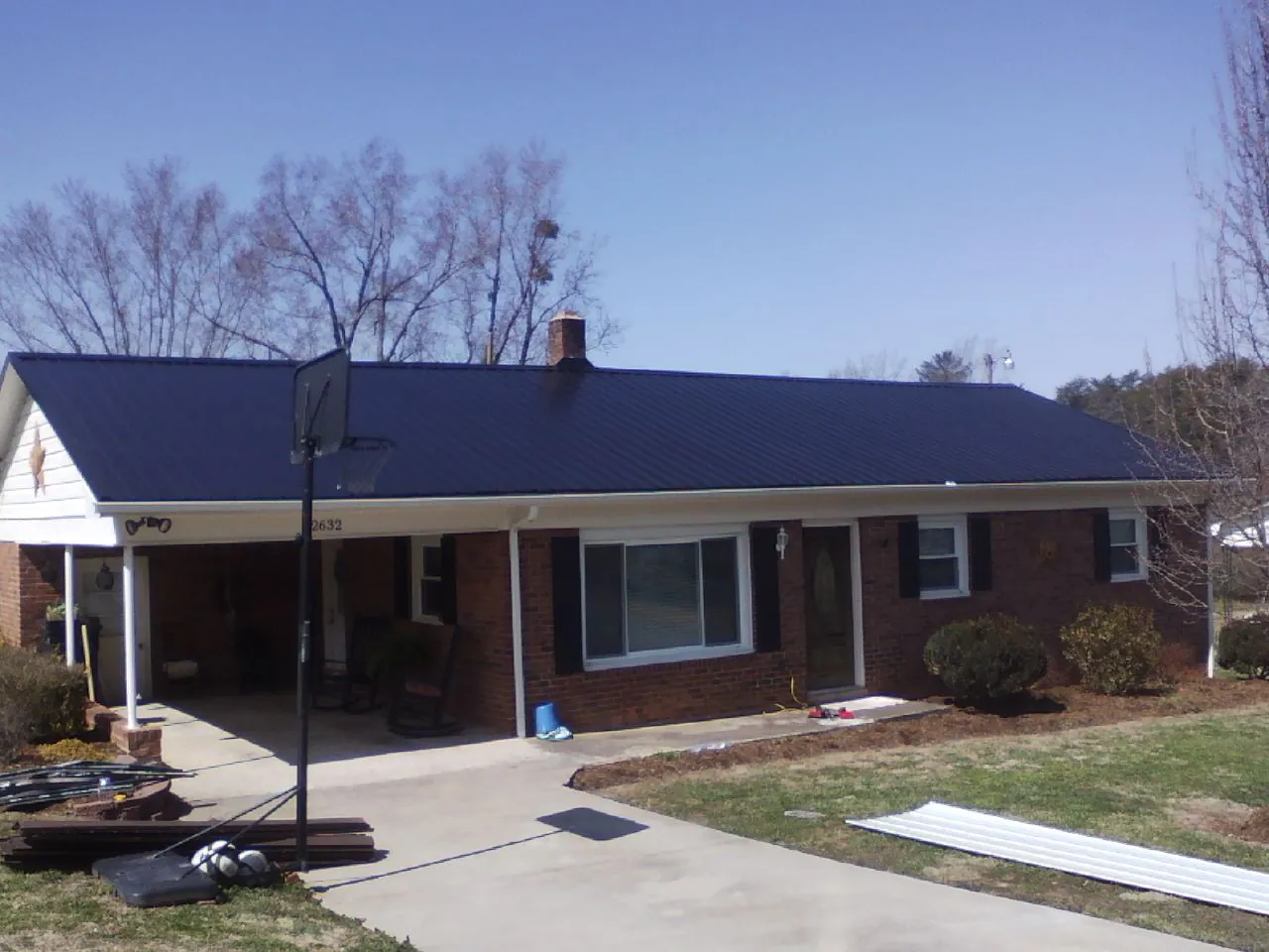 Finished dark blue metal roof on a brick ranch with a carport in Frenchburg