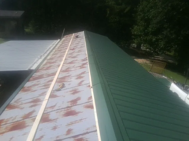 Old rusted panels beside newly installed green metal roofing — Wind Damage Roof Repair by Roofing Brothers in Frenchburg