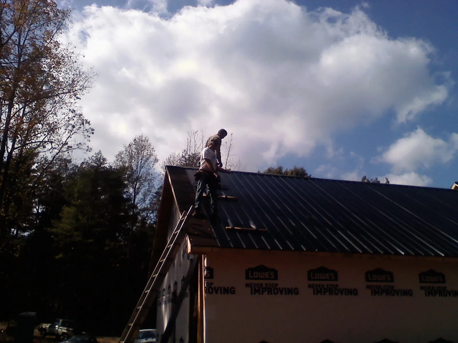 Roofer fastening dark metal panels high against a cloudy sky, from a Roof Inspection job in Frenchburg