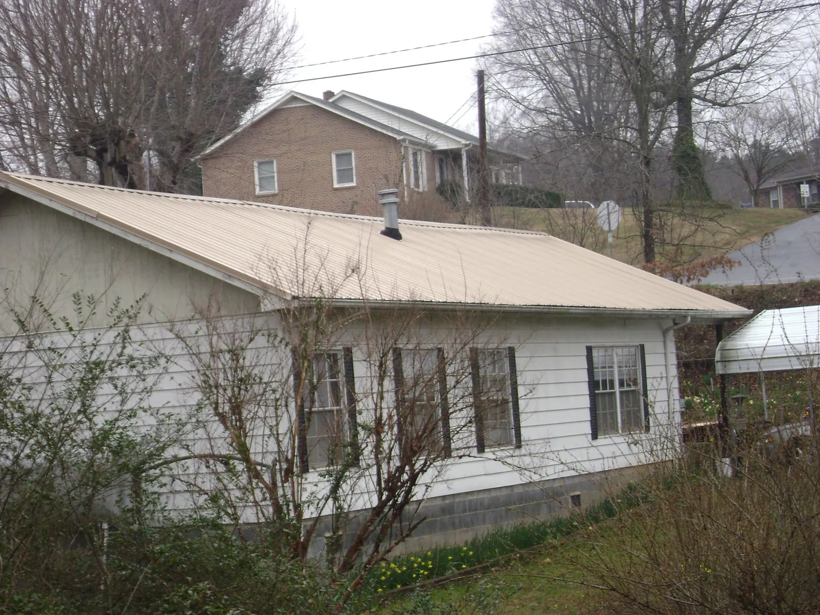 Tan metal roof on a white sided house set into a hillside — Commercial Roofing by Roofing Brothers in Frenchburg